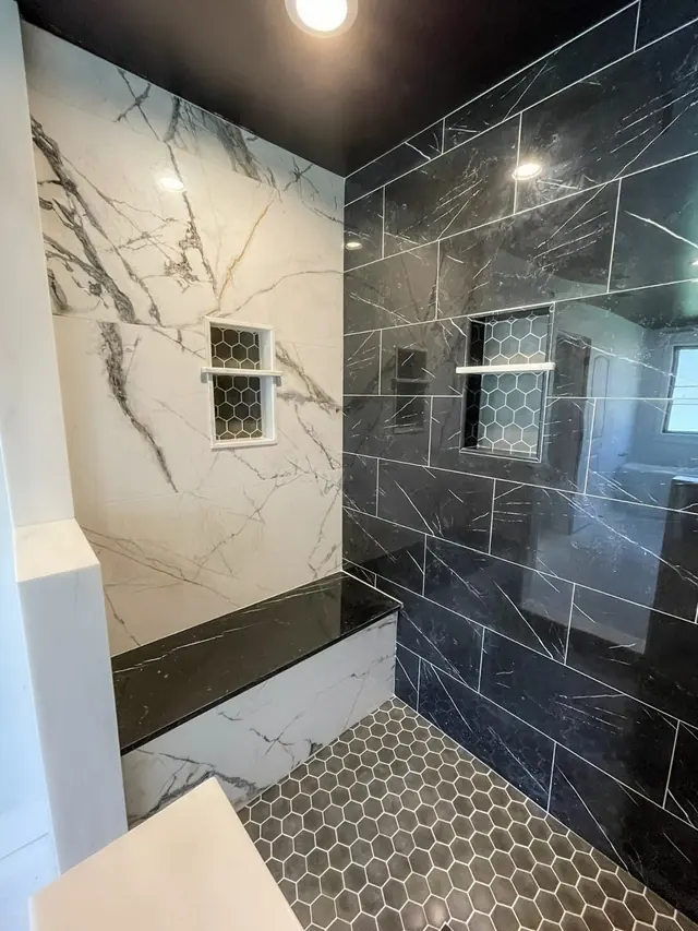 Marble and black porcelain tile shower with a built-in bench and hexagon floor, finished by Bencke's Tile