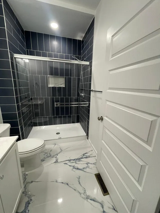 Navy tile shower and marble-look floor in a bathroom