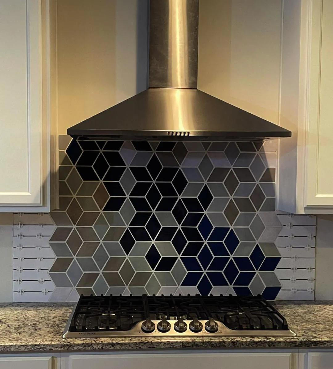 Blue, white and gray diamond tile backsplash centered behind a gas cooktop and range hood