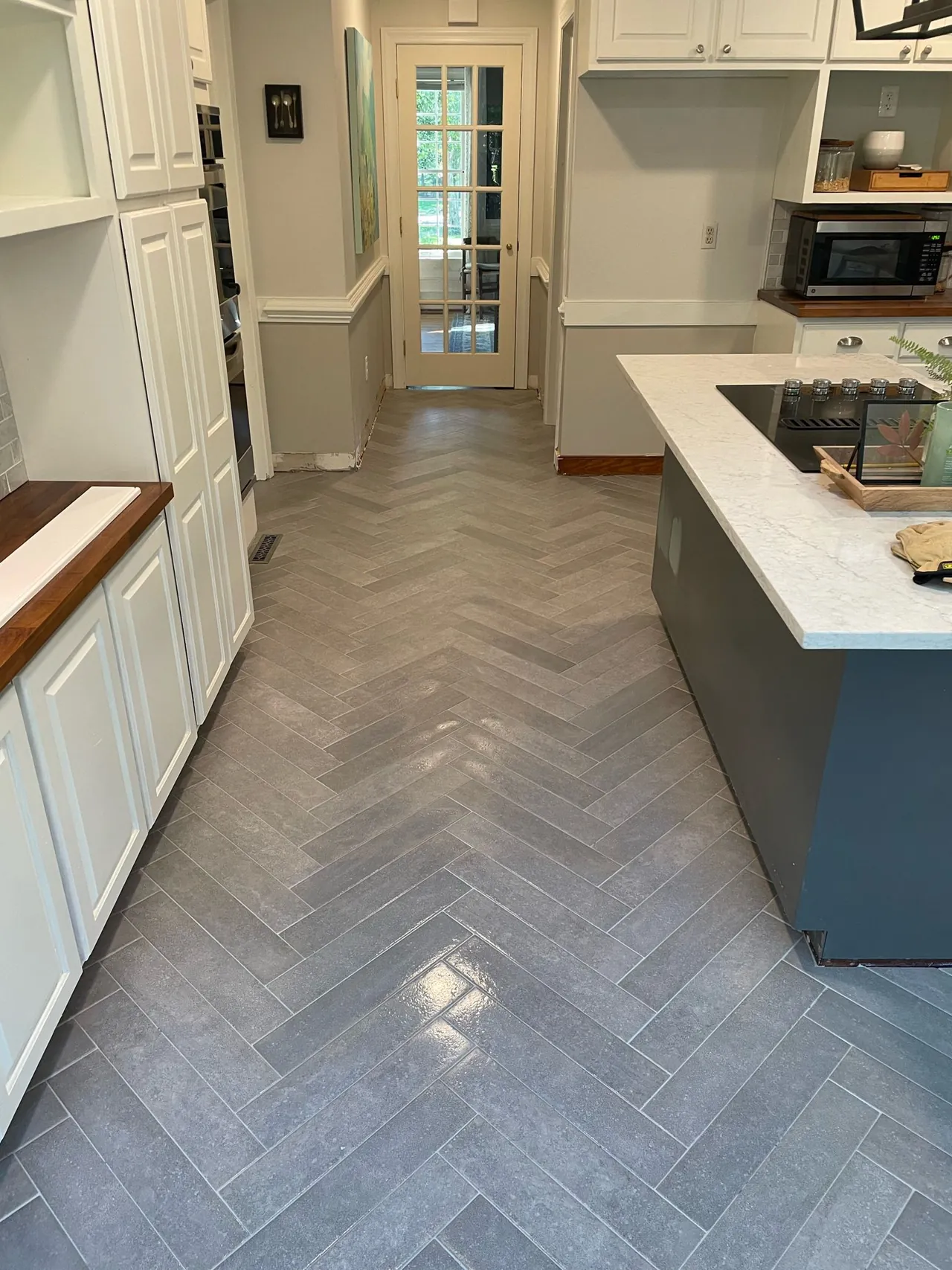 Gray herringbone tile floor running down a kitchen aisle between white cabinets and a dark island