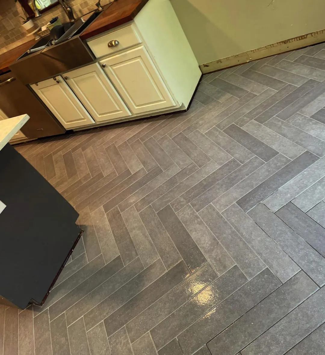 Gray herringbone floor tile laid up to white kitchen cabinets with a wood countertop