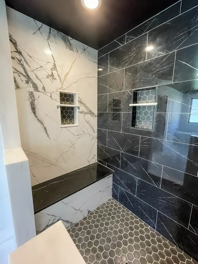 Walk-in shower with a white marble-look wall, black marble-look porcelain tile, a black bench and a gray hexagon mosaic floor, with two hexagon-tile niches
