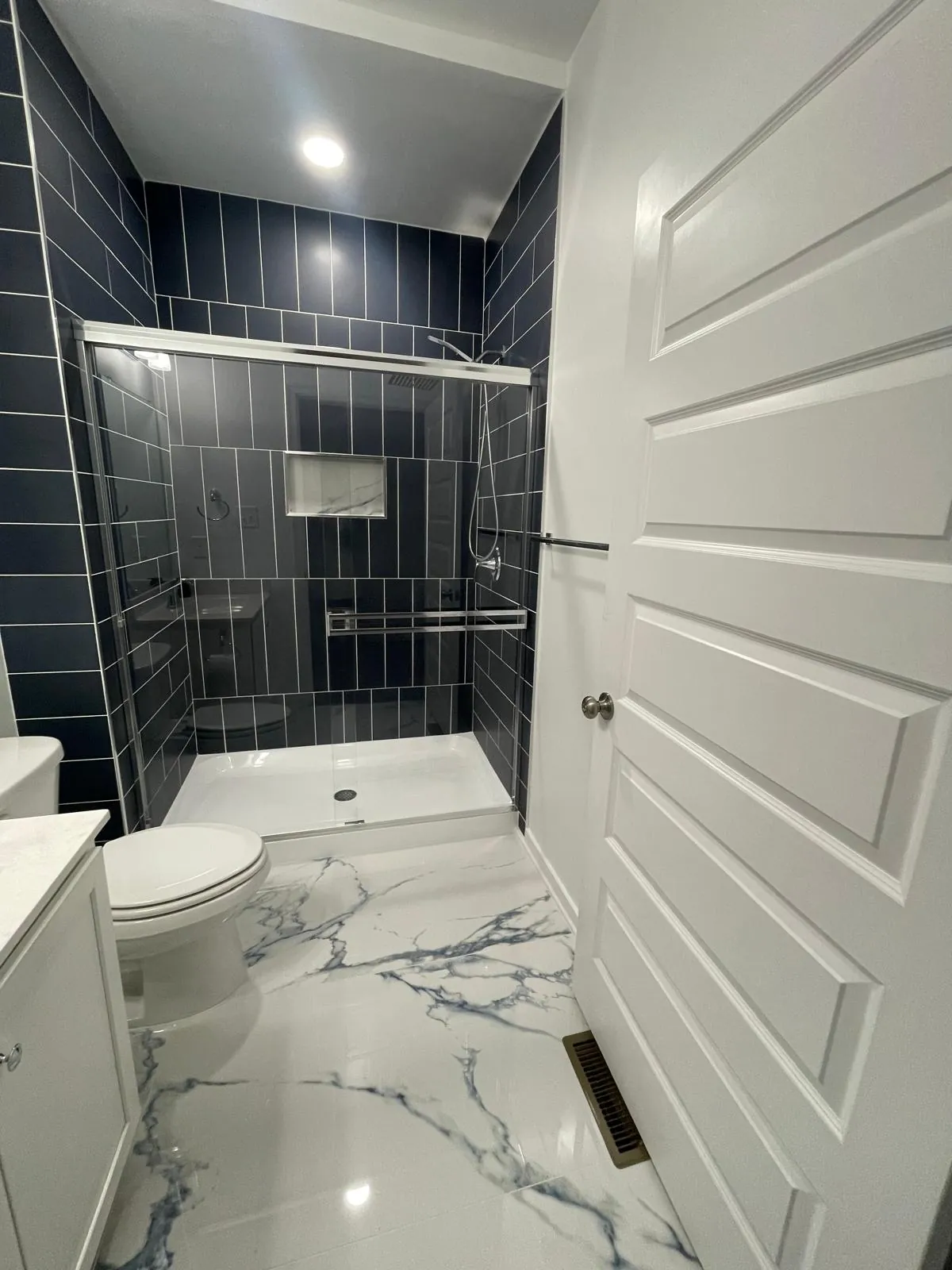 Small bathroom with navy tile shower walls, a glass shower door, a white vanity and a marble-look floor with blue veining