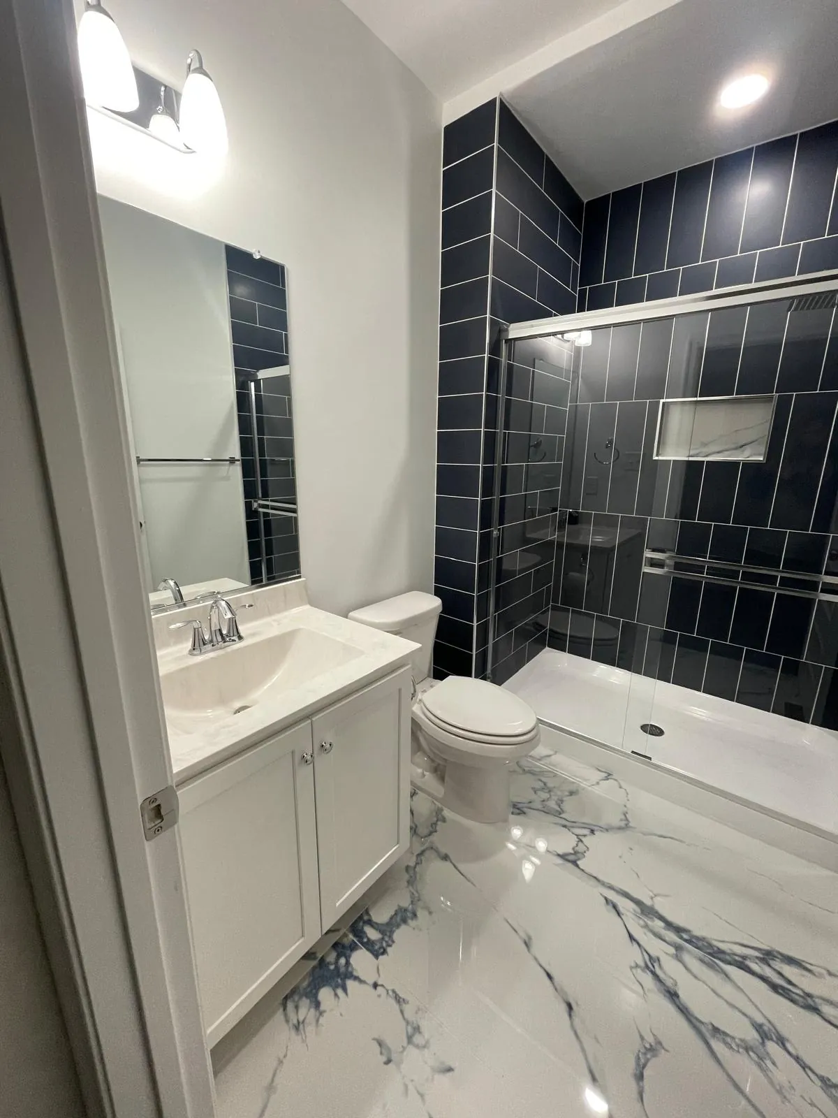 Bathroom vanity beside a navy tile shower with a sliding glass door and a glossy marble-look floor