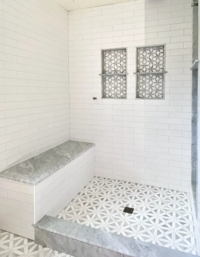 White subway tile shower with a stone bench, two patterned mosaic niches and a star-pattern mosaic floor