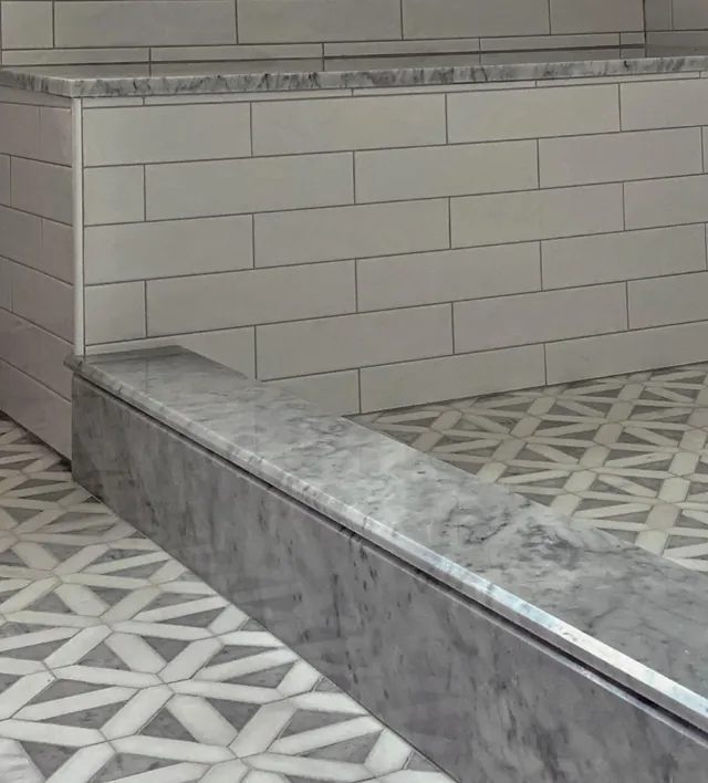 Close view of a gray marble shower bench and curb against large white wall tile, with a star-pattern mosaic floor