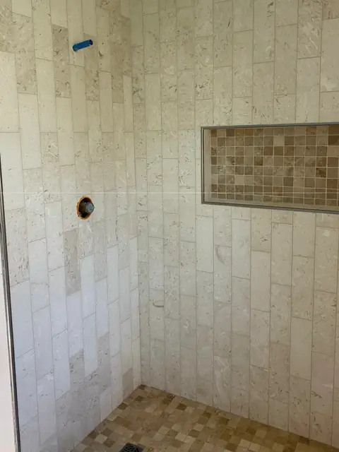 Travertine-look tile shower with a mosaic niche
