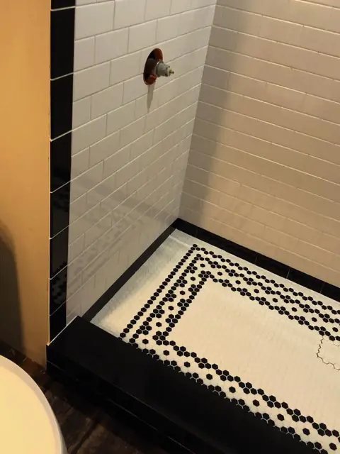 Shower with a black and white penny tile floor border