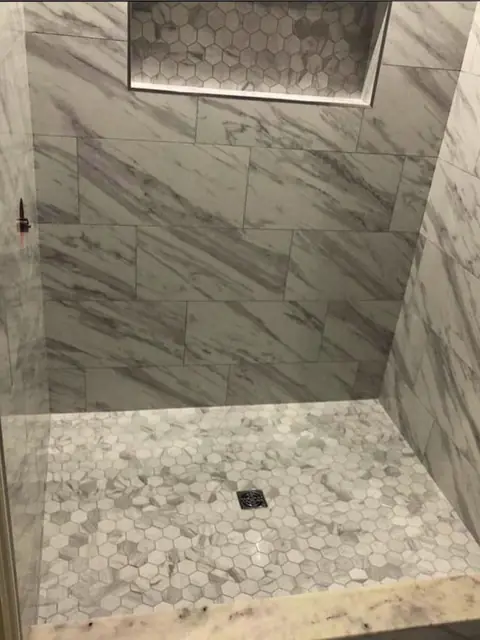 Marble-look tile shower with a hexagon floor and a lit niche