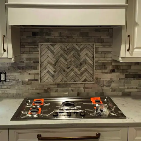 Gray herringbone tile backsplash behind a cooktop