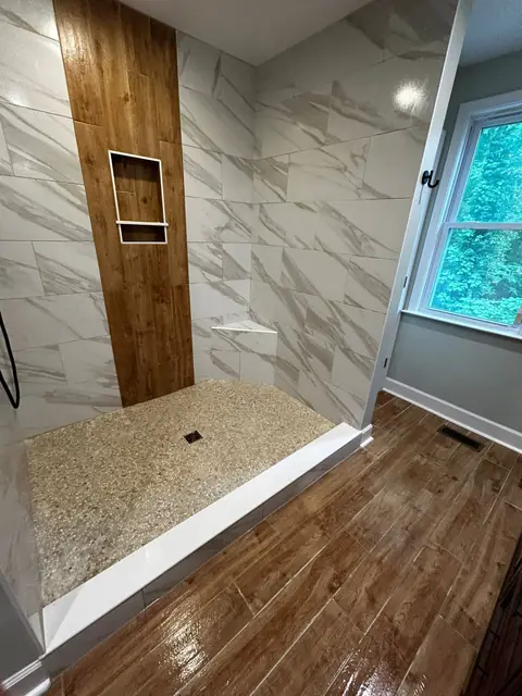 Marble-look tile shower with a wood-look accent strip and a pebble floor
